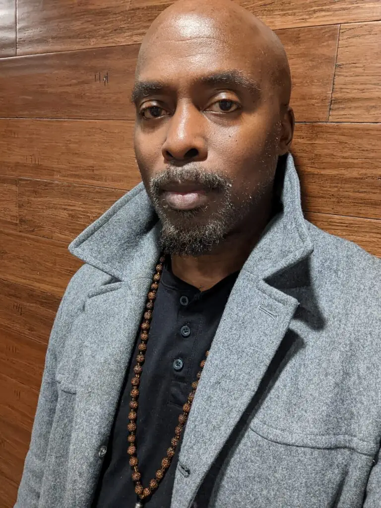 Edward Newbins in a grey coat against a wood wall.